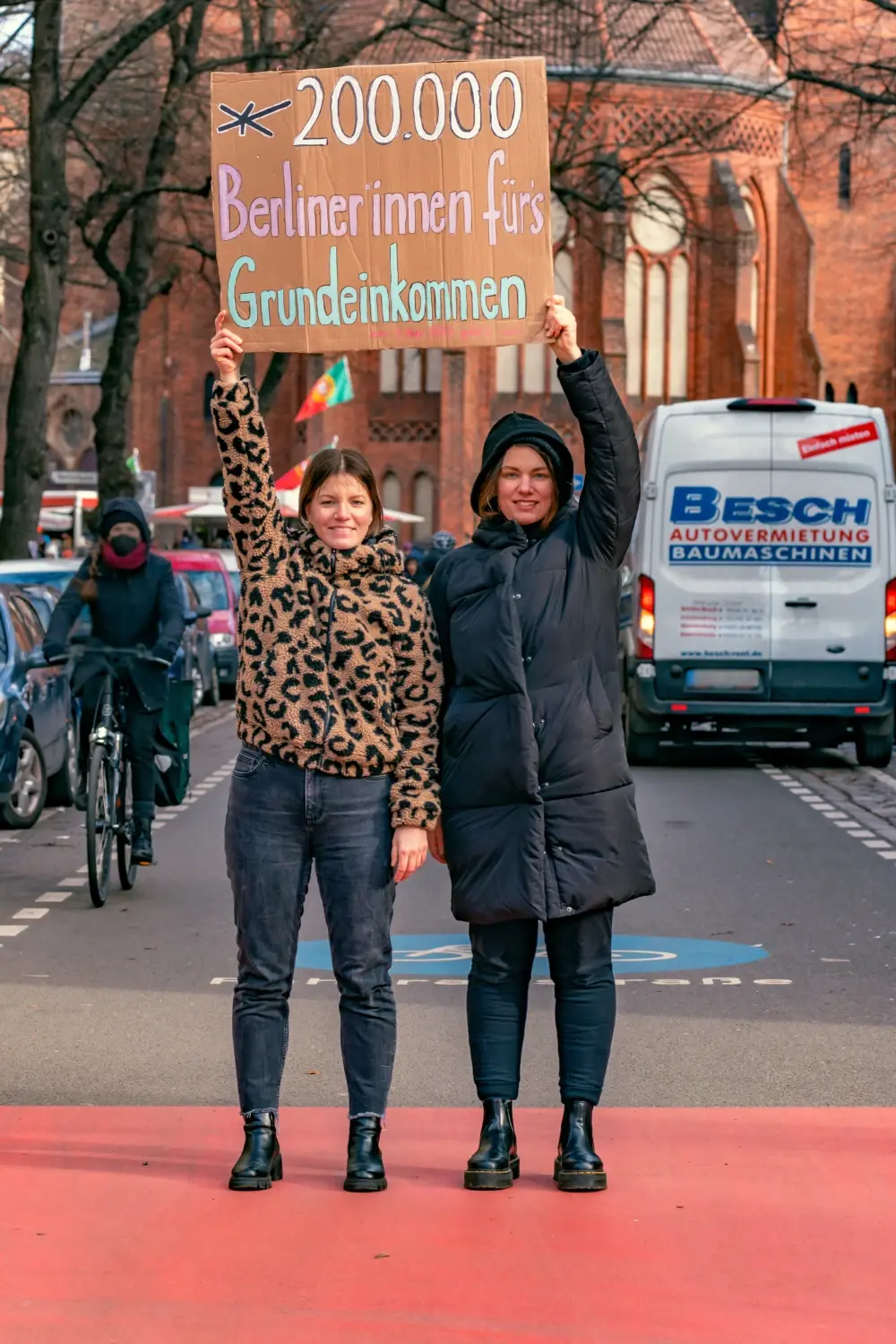 2 Mitglieder der Expedition Grundeinkommen halten ein Plakat mit der Aufschrift "200.000 Berliner innen fürs Grundeinkommen"